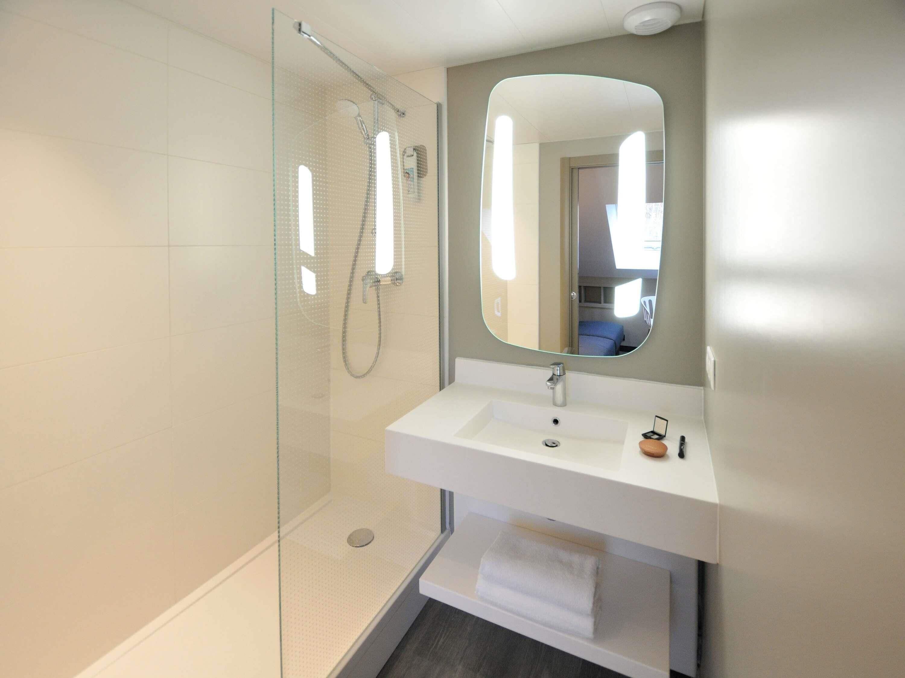 A modern bathroom with a glass shower enclosure, a white sink, and a mirror.