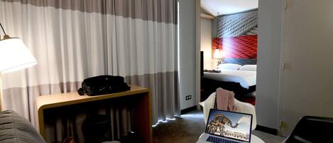 A hotel room with a bed, a desk with a laptop, a chair, and a couch.