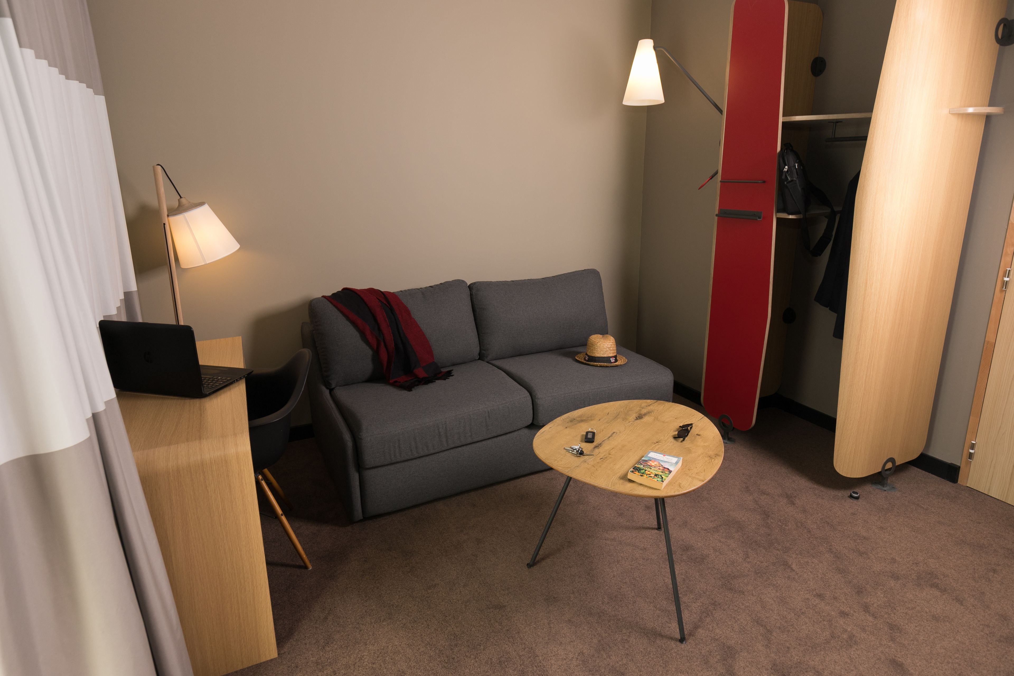 A compact room with a grey sofa, a small round table, a lamp, and a closet with a red door.