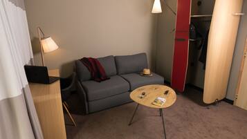 A compact room with a grey sofa, a small round table, a lamp, and a closet with a red door.