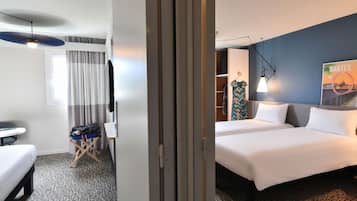 A hotel room with a bed, a desk, a chair, a wardrobe, and a poster on the wall.