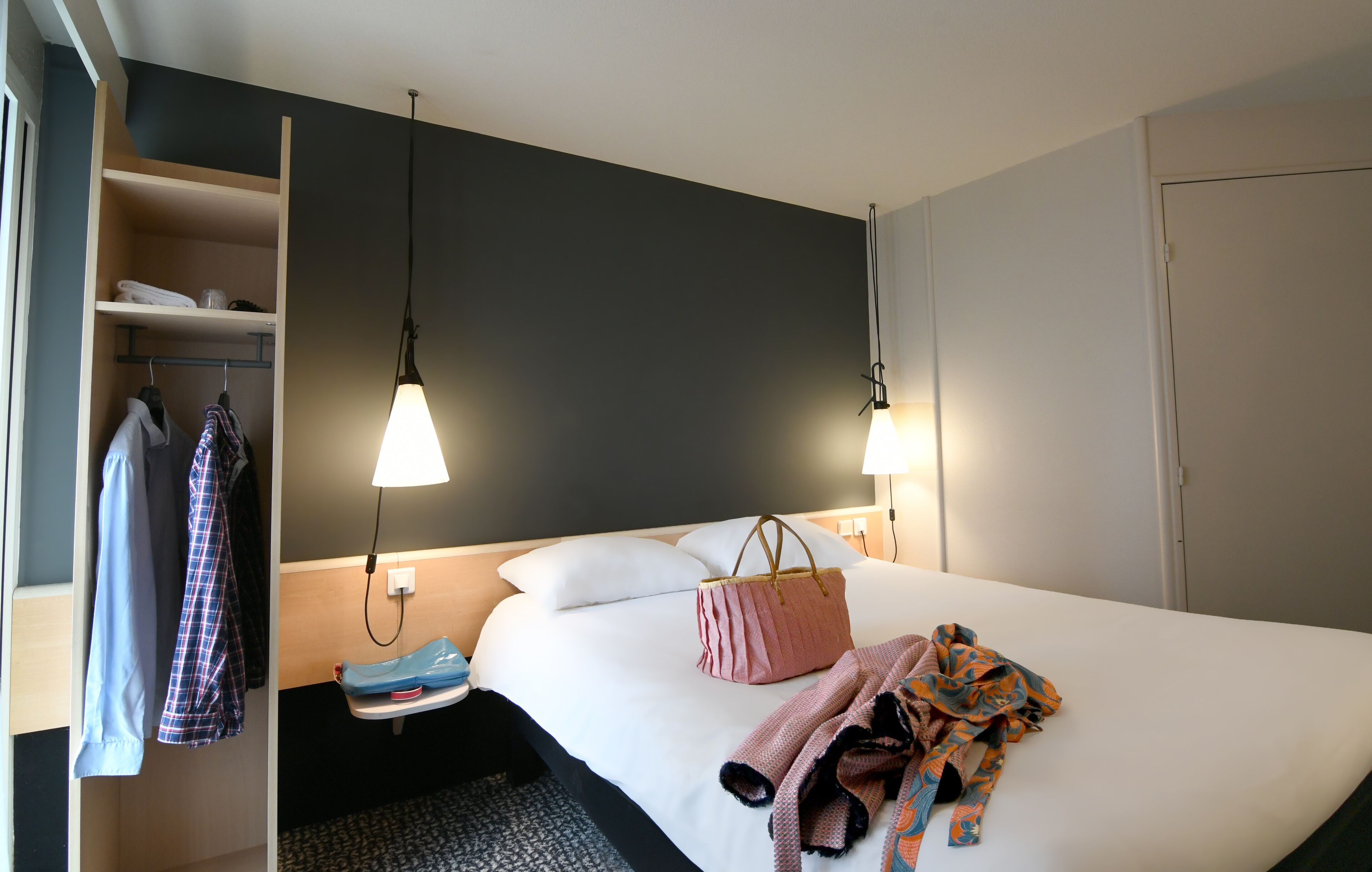 Una habitación de hotel con cama, armario, mesita de noche y dos lámparas de pared.