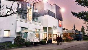 Ein modernes Hotel mit einem gut sichtbaren 'ibis'-Schild, Außenplätzen und einem Balkon.