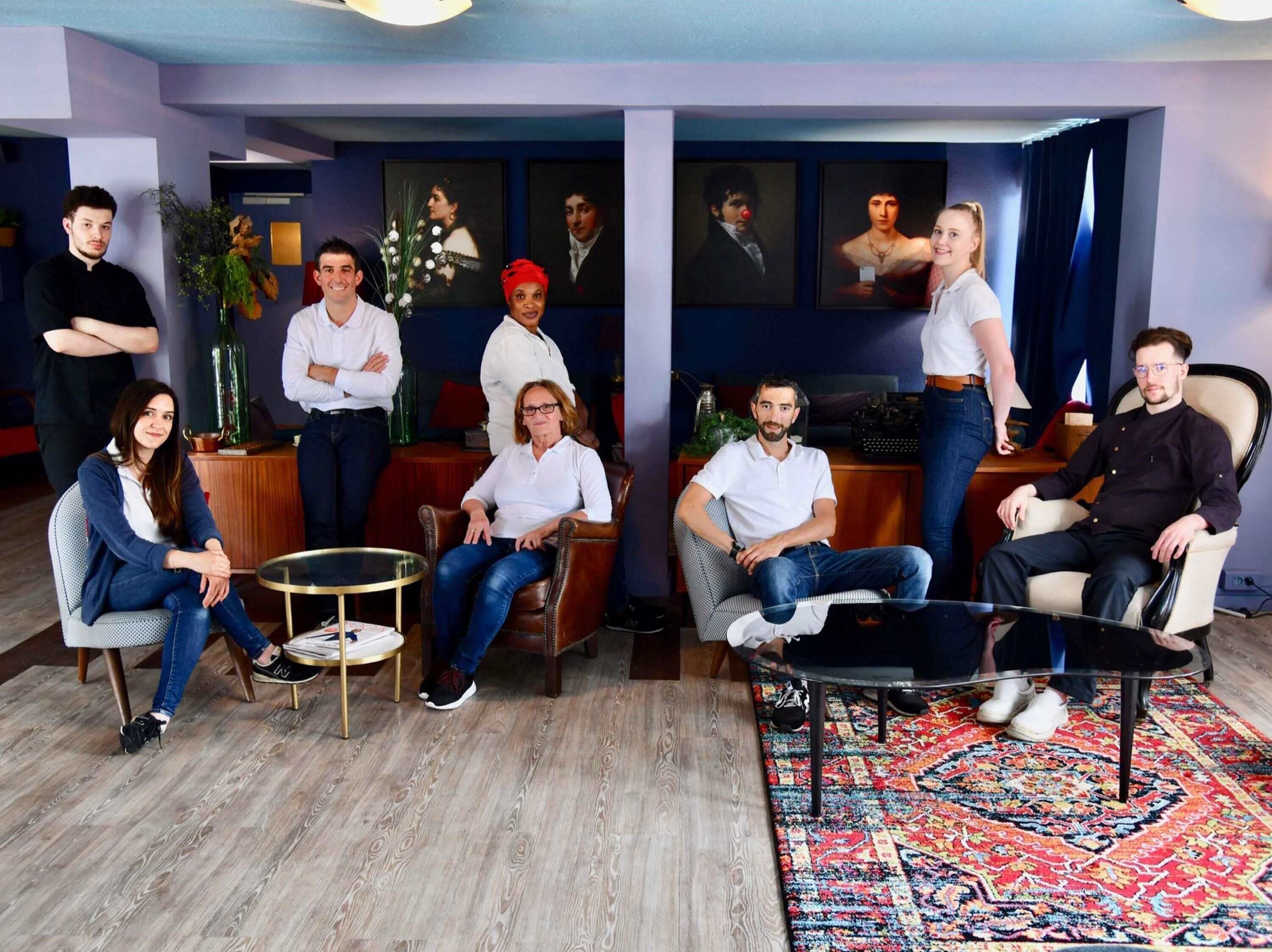 Een groep mensen in een modern interieur met een houten vloer, een ronde tafel en een vloerkleed met een patroon.
