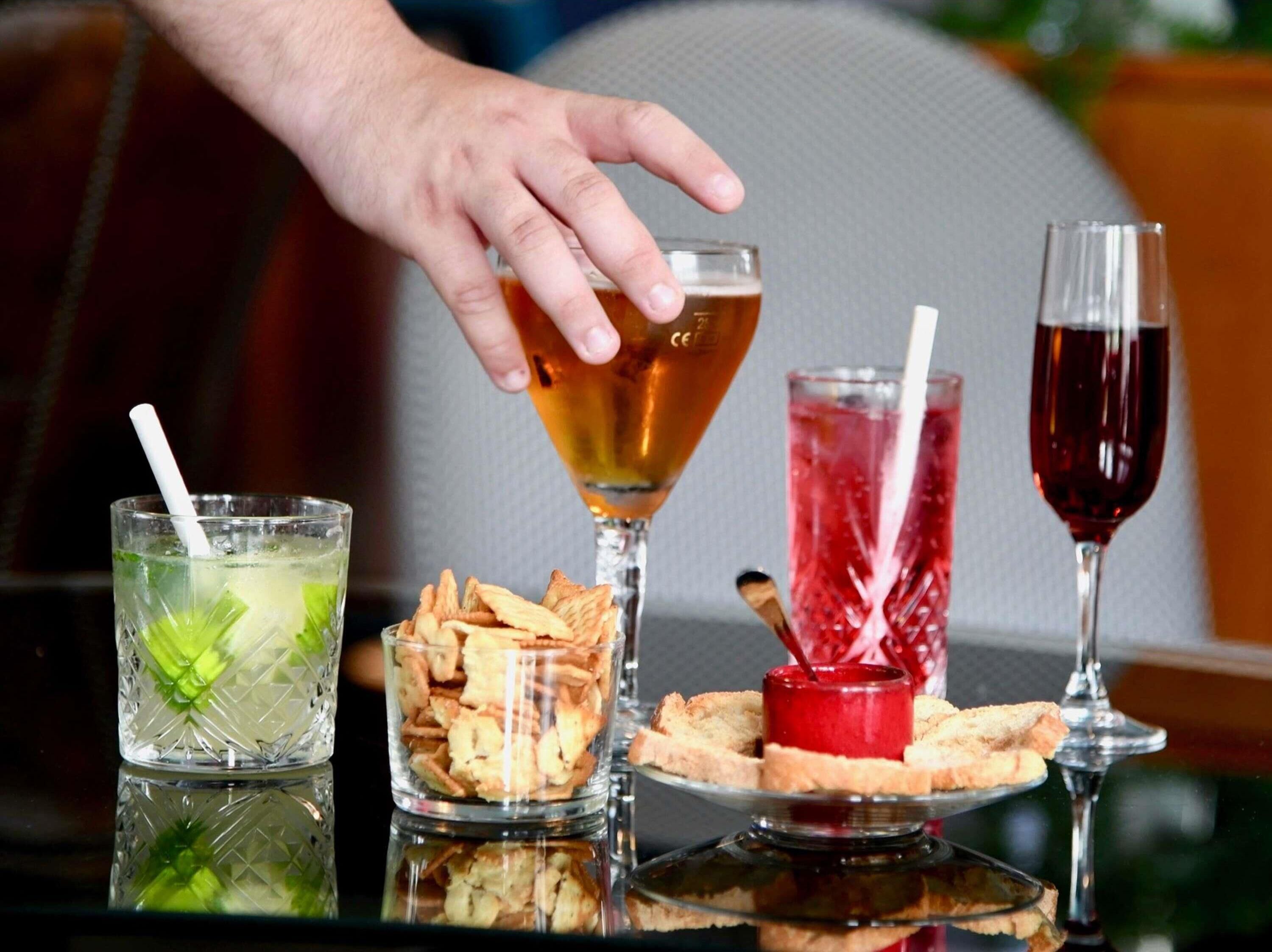 Una mesa con diversas bebidas y aperitivos, incluyendo una copa de martini, un vaso alto con una bebida roja y un vaso con una bebida verde.