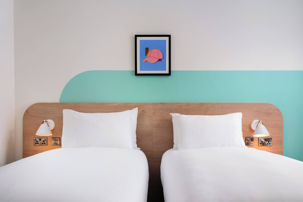 A double bed with white bedding, two bedside lamps, and a framed picture on the wall.