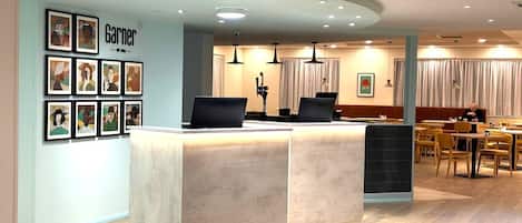 A modern reception area with a counter, framed artwork on the wall, and a seating area with tables and chairs.