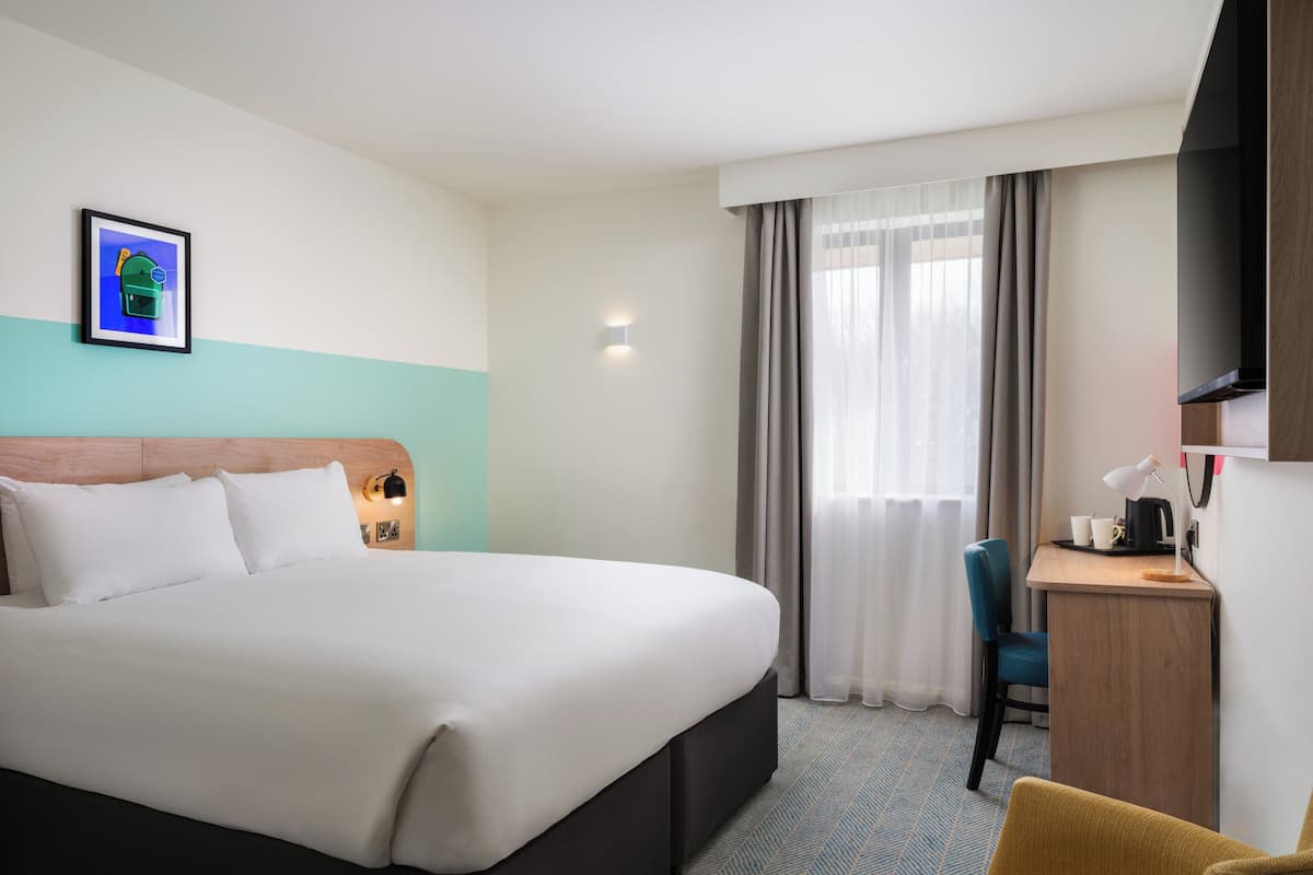A hotel room with a large bed, a desk with a chair, a television, and a window with curtains.