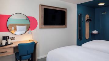 Une chambre d’hôtel équipée d’un bureau, d’une chaise, de deux lits, d’une télévision, d’un miroir et d’un espace douche.