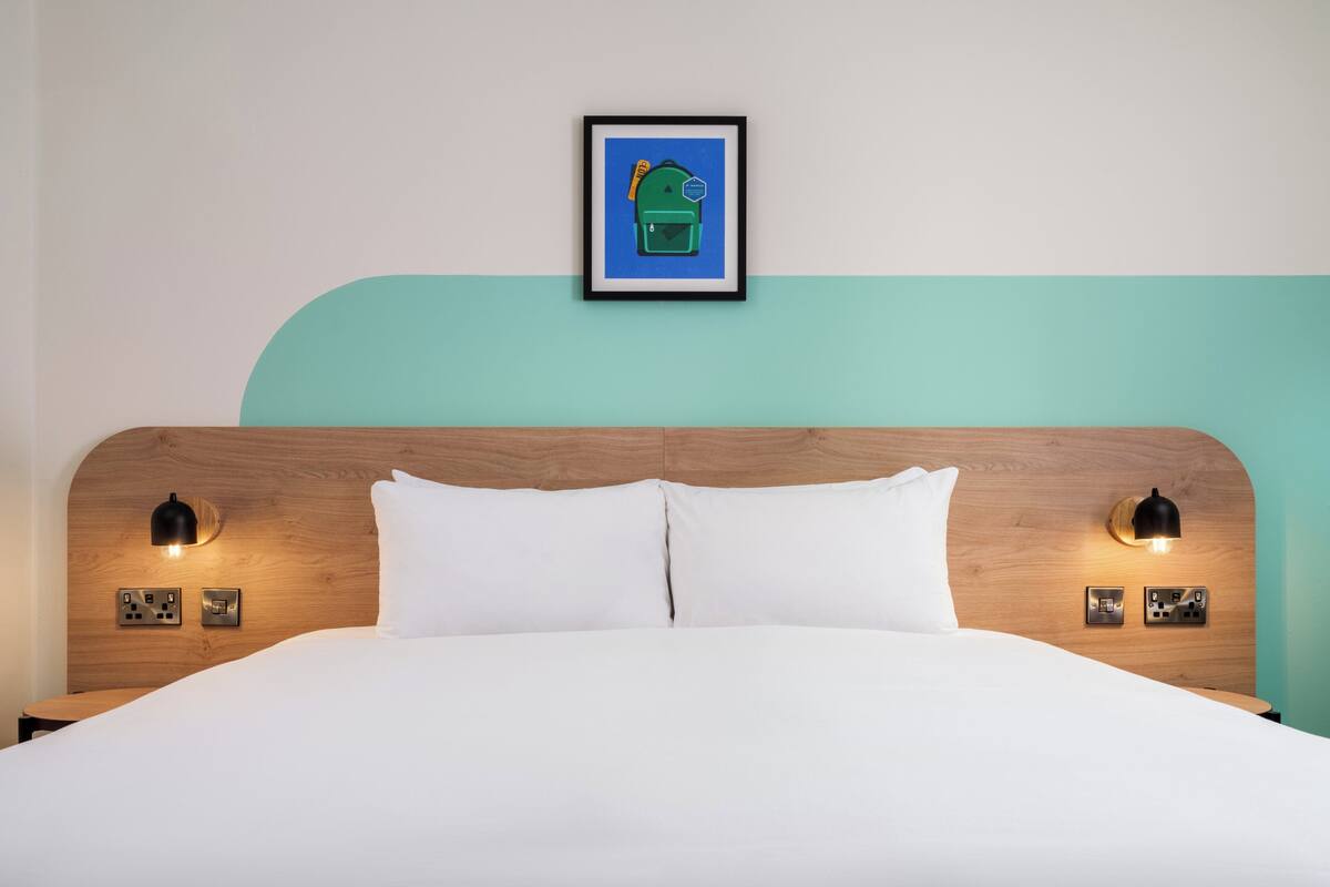 A neatly made bed with white linens, a wooden headboard, and two wall-mounted reading lamps.