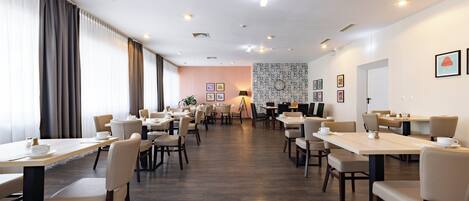 Un comedor amplio con varias mesas y sillas, un papel tapiz decorativo y una puerta al fondo.