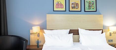 A hotel room with two beds, a wooden headboard, bedside lamps, a desk with a chair, and three framed pictures on the wall.