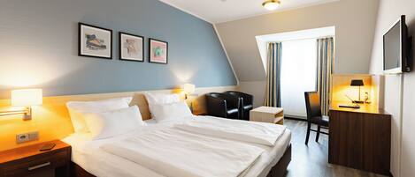 Une chambre d’hôtel avec un grand lit, des tables de chevet, un bureau avec une chaise, une télévision et des tableaux encadrés au mur.