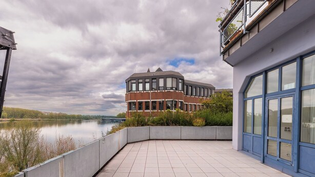 A modern building with large windows and a curved balcony overlooking a body of water.