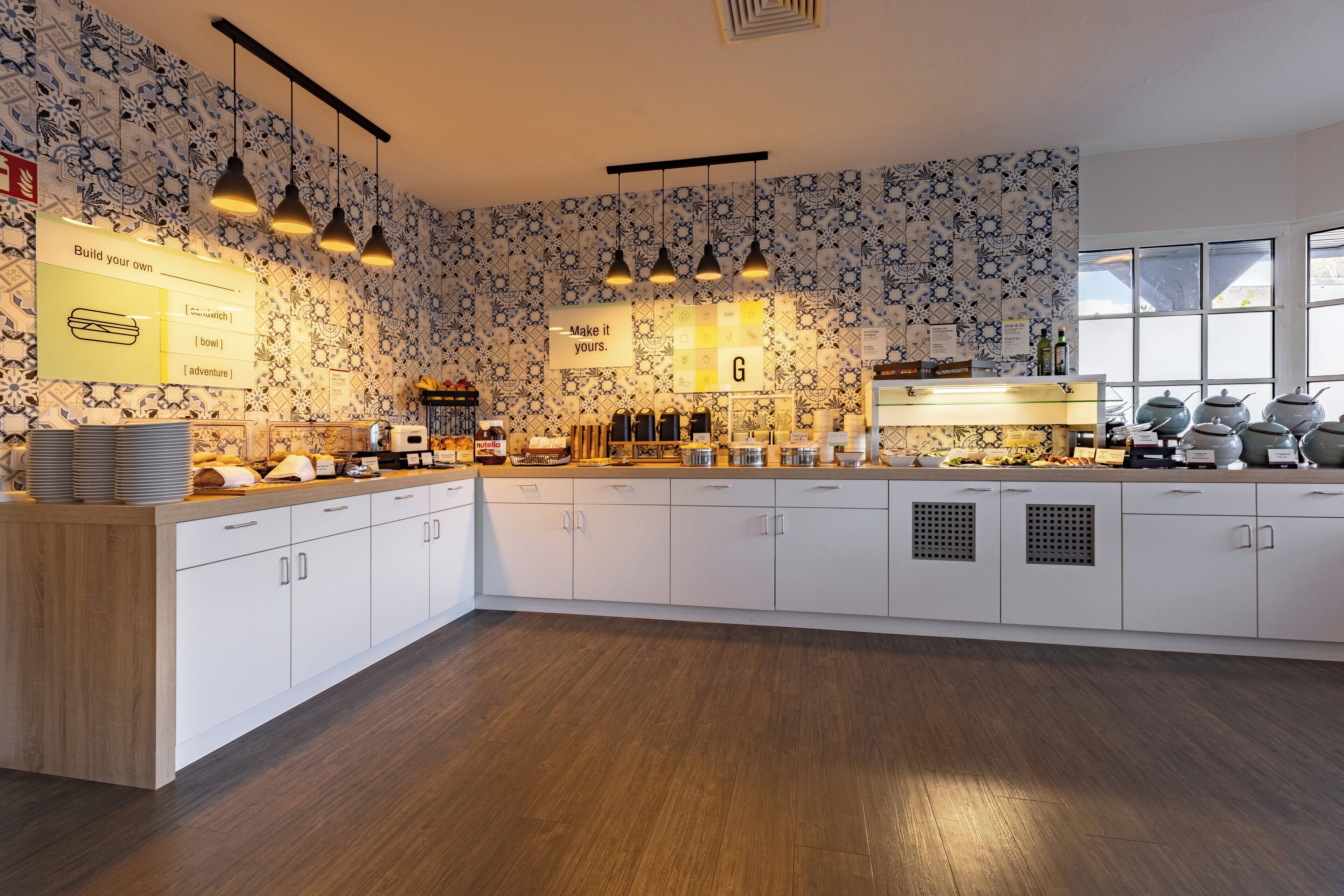 A modern kitchen with white cabinetry, patterned wallpaper, and pendant lighting.