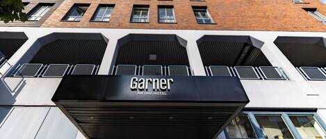 Entrada de un hotel con fachada moderna, grandes ventanales y un cartel llamativo que dice 'Garnier An IHG Hotel'.