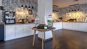 A modern kitchen with white cabinets, a central island, hanging pendant lights, and a coffee station.