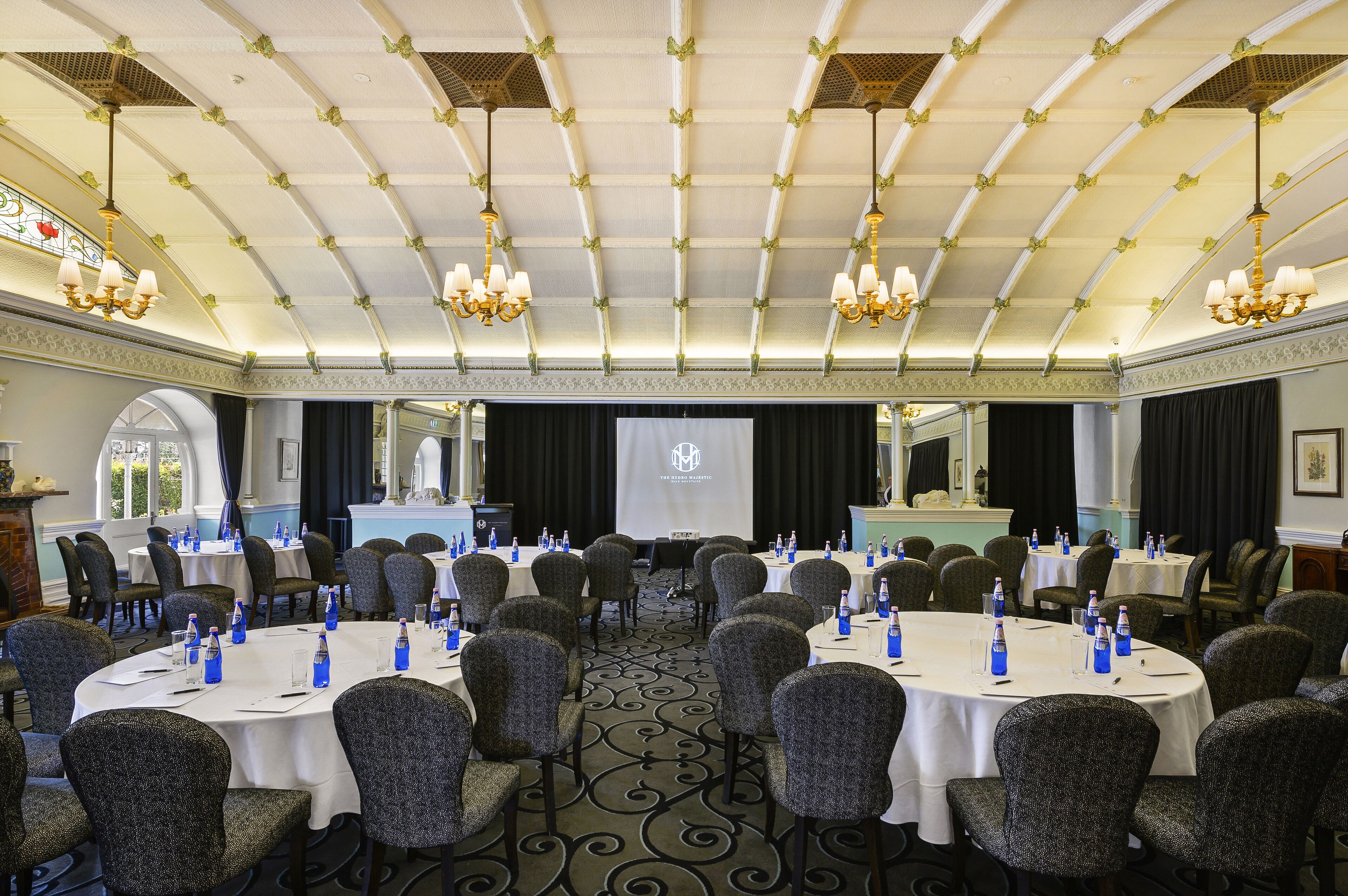 A conference room with round tables, chairs, and a projector screen.