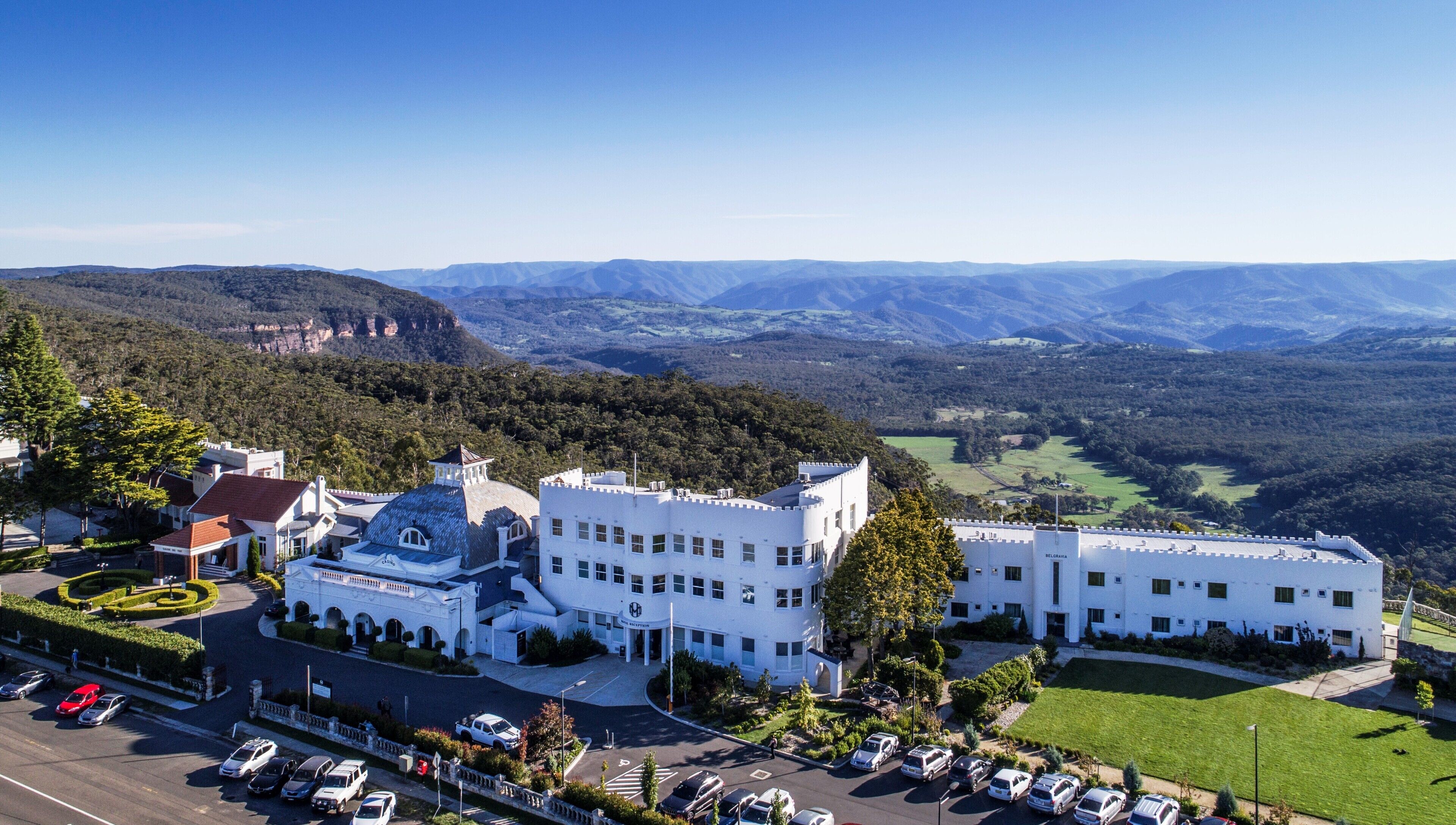 A large, white building with a unique architectural design, surrounded by lush greenery and mountains in the background.