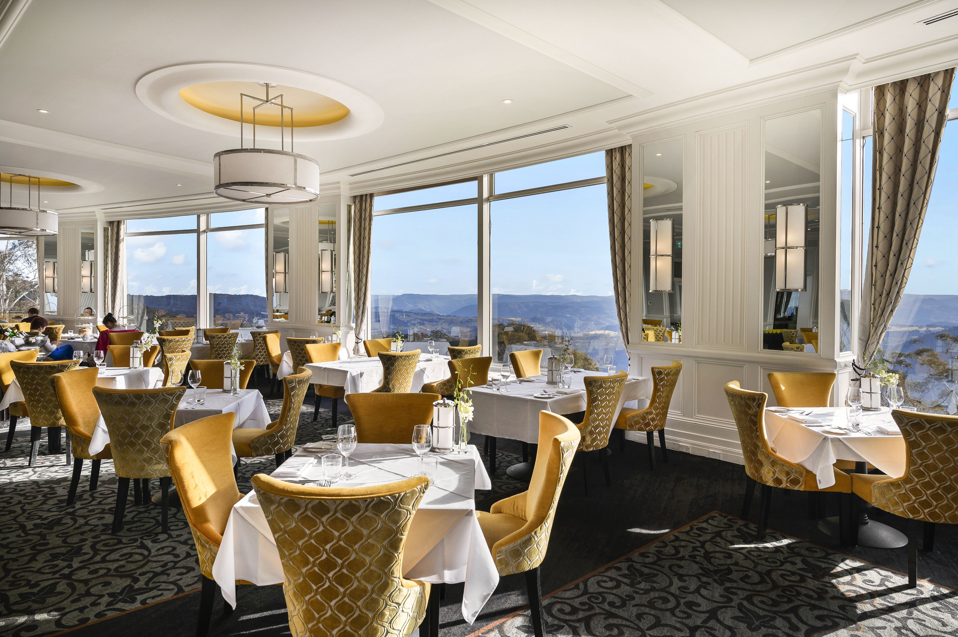 A restaurant with tables and chairs, large windows, and a view of the mountains.