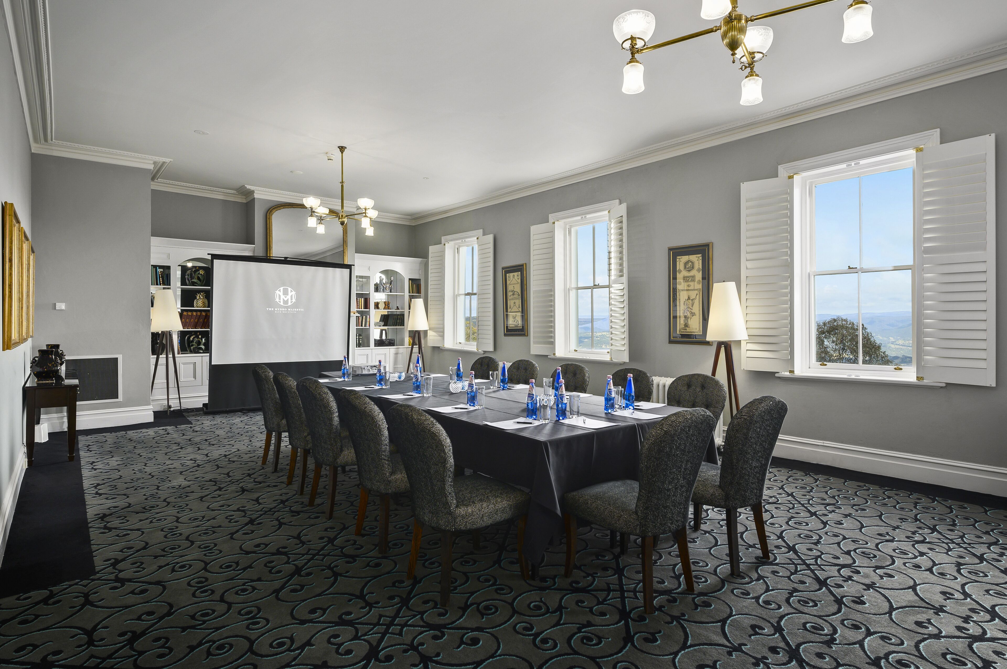 A conference room with a long table, chairs, and a projector screen.