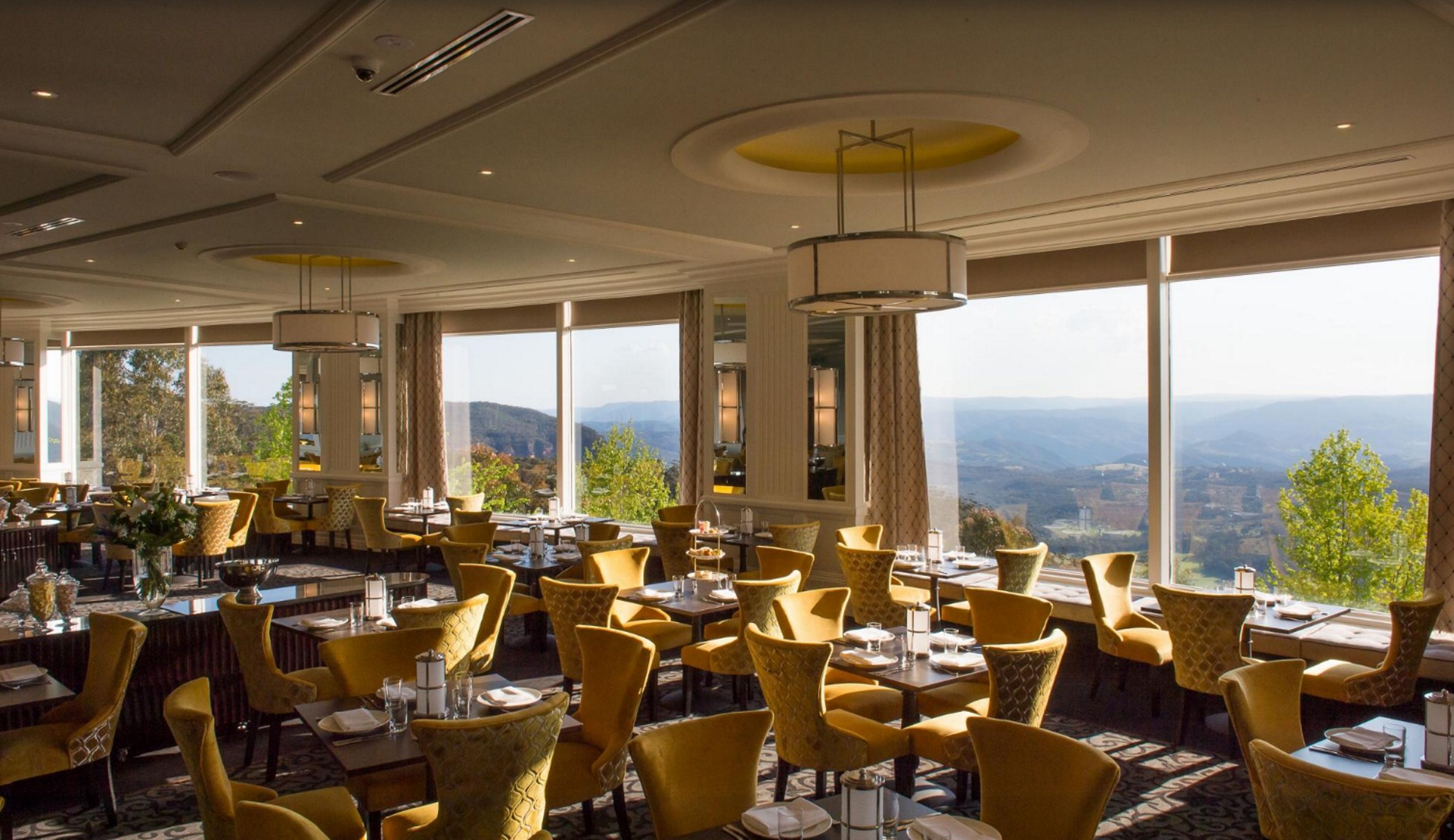 A restaurant with yellow chairs, large windows, and a view of the mountains.