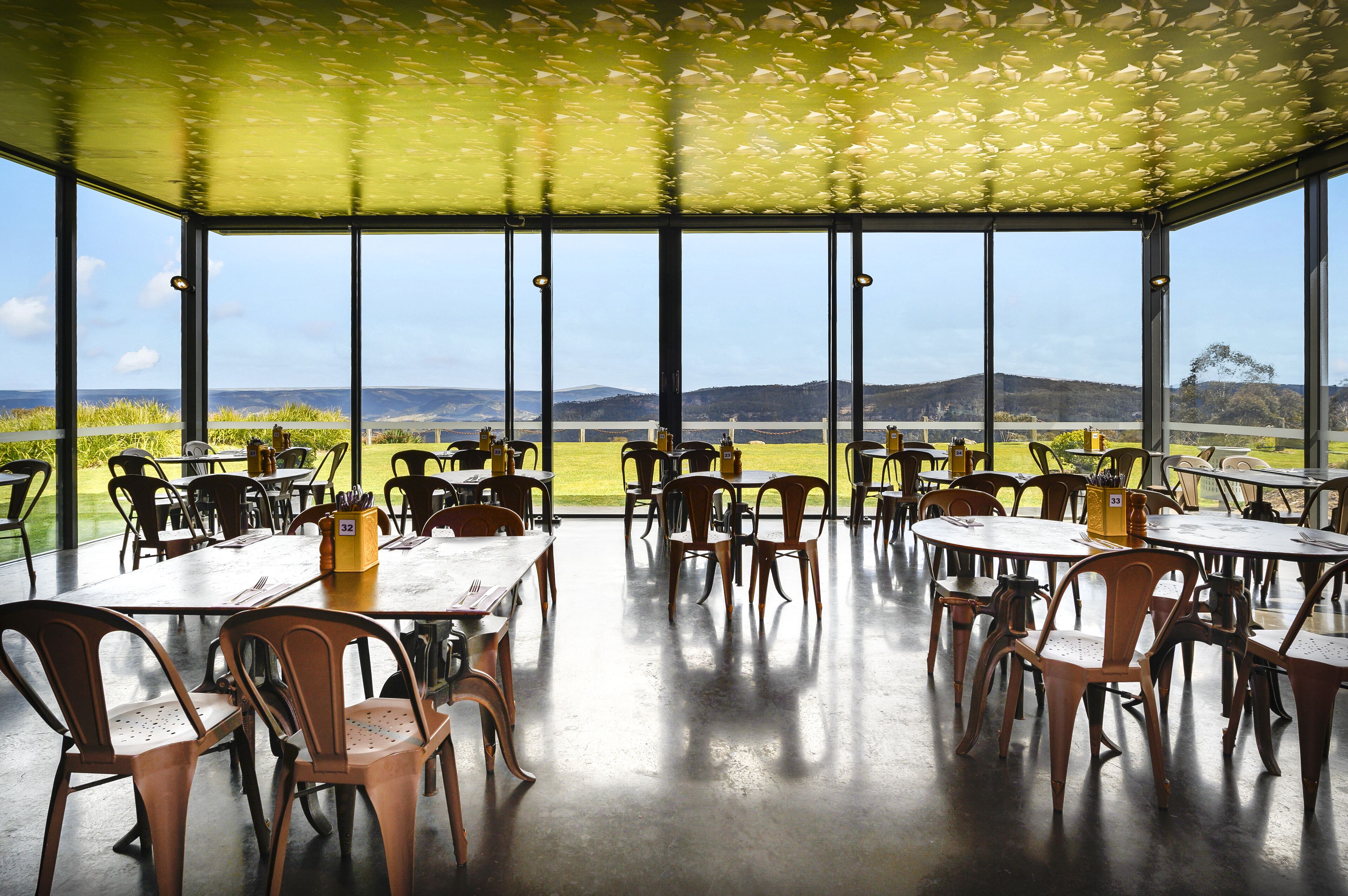 Un espace de restauration intérieur avec des tables et des chaises, de grandes fenêtres et une vue sur la campagne.