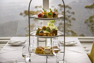 Una bandeja escalonada con varios pasteles y un vaso de agua sobre una mesa con mantel blanco.