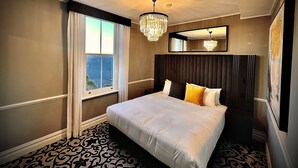 Een hotelkamer met een groot bed, een kroonluchter, een raam met gordijnen en een spiegel aan de muur.
