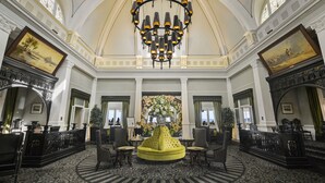 Een statige lobby met een centraal, rond zitgedeelte, een grote kroonluchter en een bloemstuk.