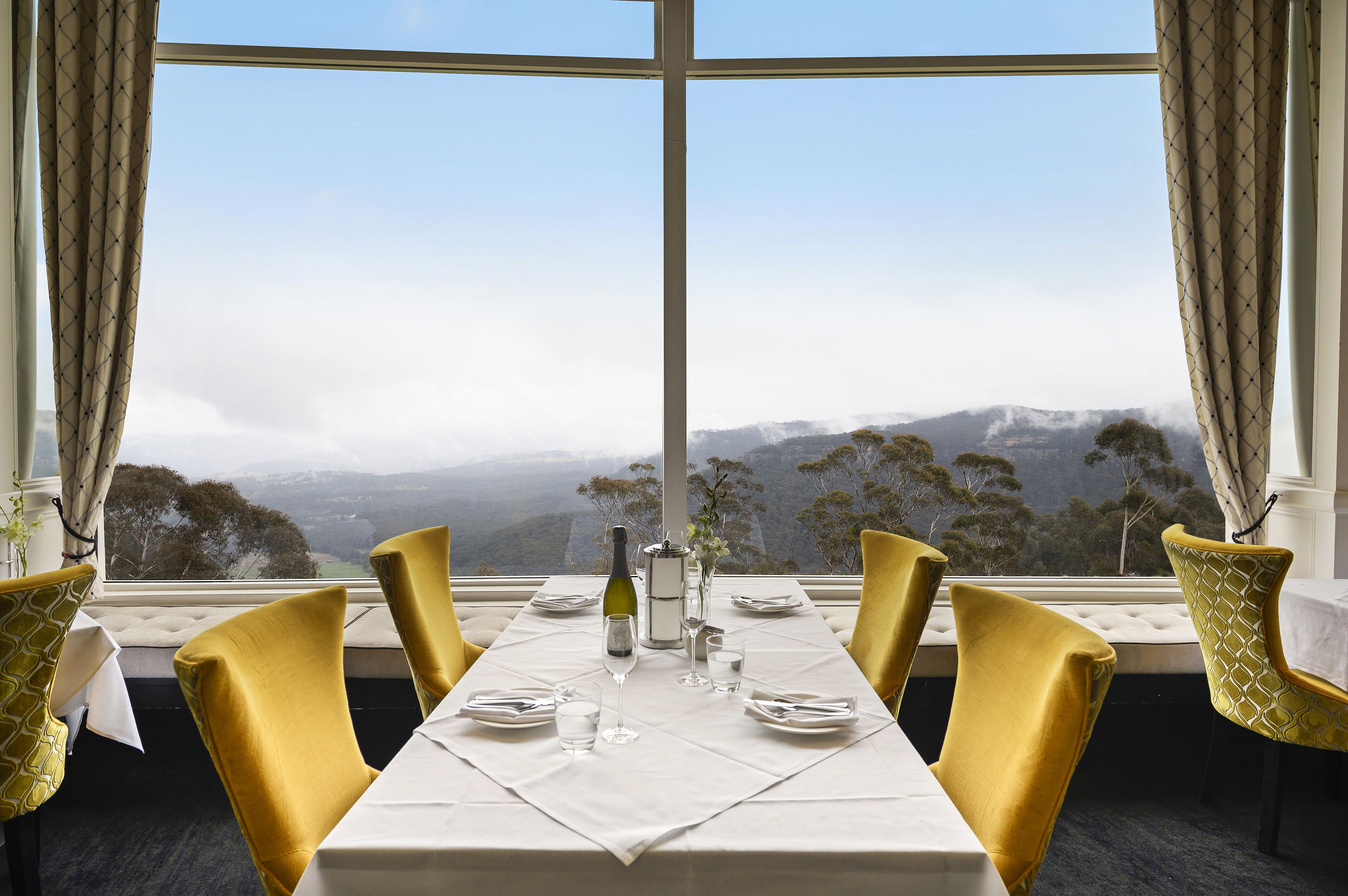 A dining table set for four with a view of a mountainous landscape through large windows.
