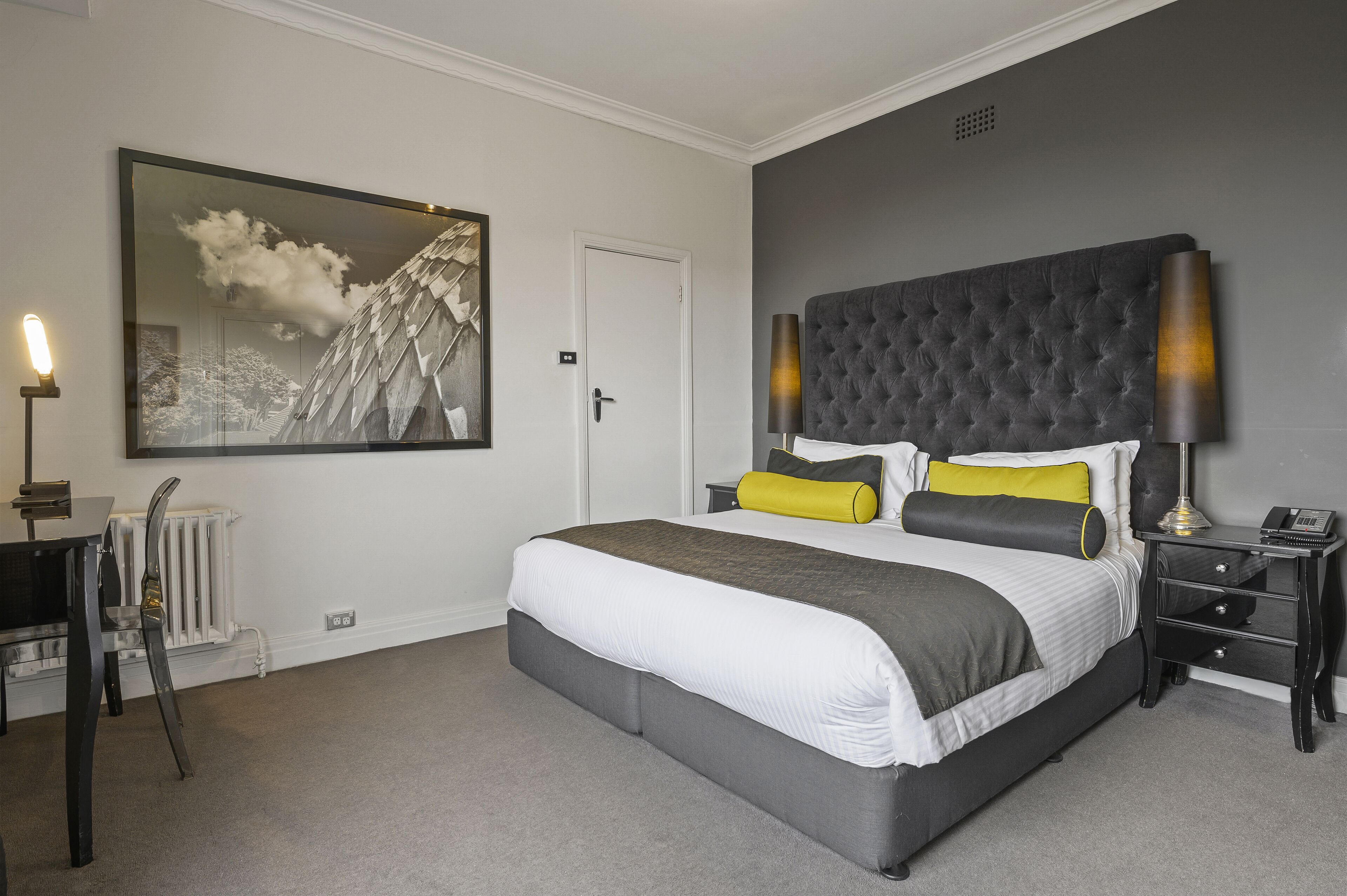 Une chambre à coucher avec un grand lit, une table de chevet, une lampe, une chaise et un grand tableau encadré au mur.