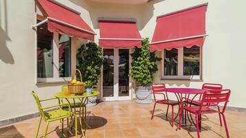 Une terrasse avec une table et des chaises, une plante en pot et un panier rempli de fruits.