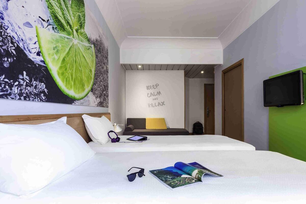 Une chambre d’hôtel moderne, équipée d’un lit, d’un téléviseur fixé au mur et d’une citation inspirante sur le mur.