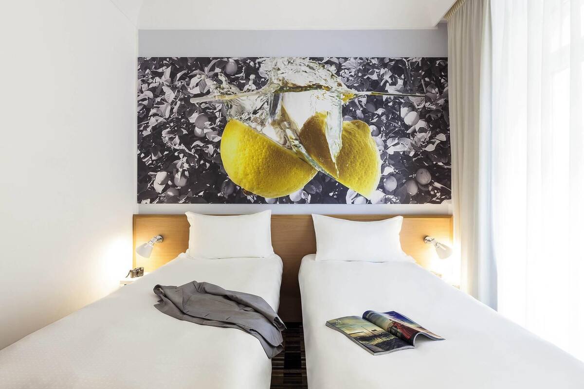 Une chambre d’hôtel avec deux lits, une grande peinture abstraite et un magazine posé sur le lit de droite.