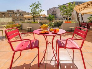 A patio with red metal chairs and a round table, a basket of bread, a glass of orange juice, and a fruit bowl. - ibis Styles Napoli Garibaldi (Naples)