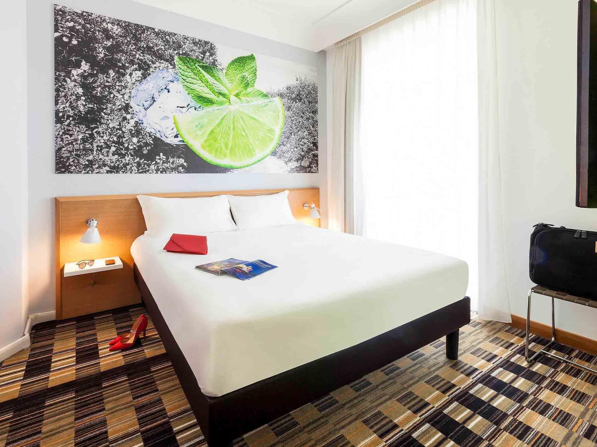 A hotel room with a bed, a nightstand with a lamp, a television, and a patterned carpet.