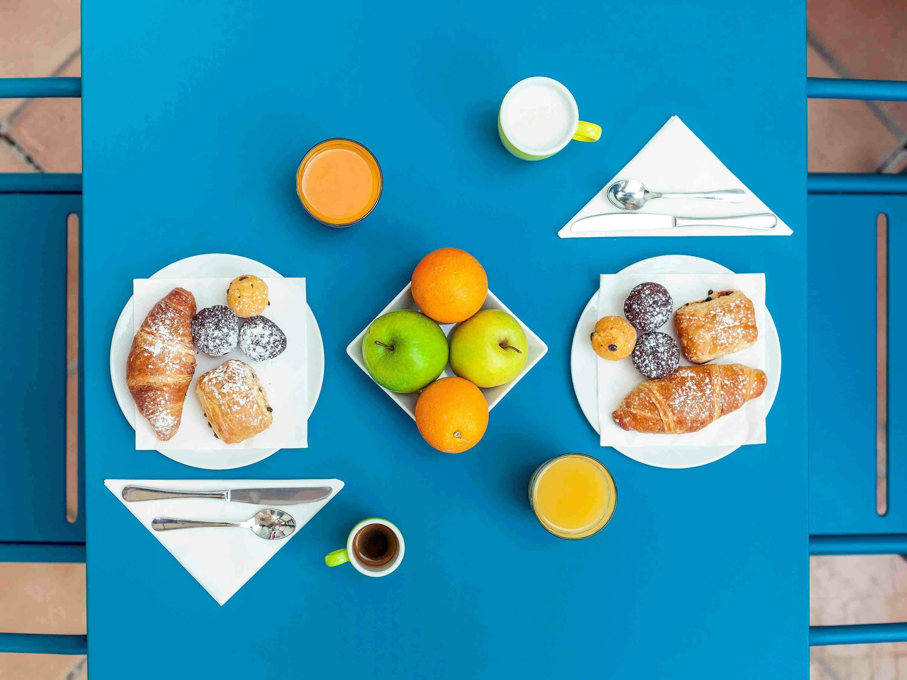 A table with plates of pastries, fruits, and beverages.