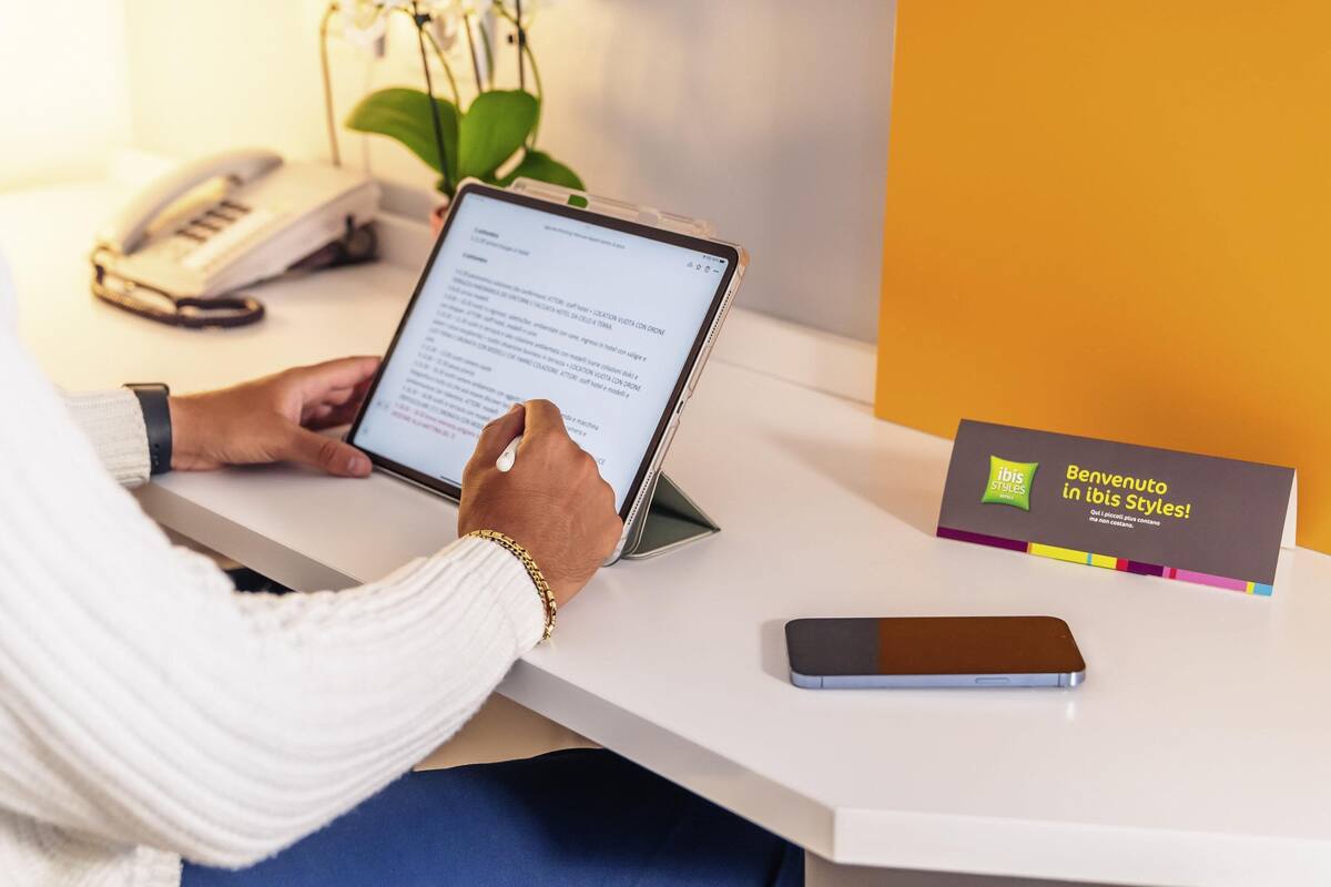 Eine Person am Schreibtisch mit einem Tablet, einem Smartphone und einer Visitenkarte.