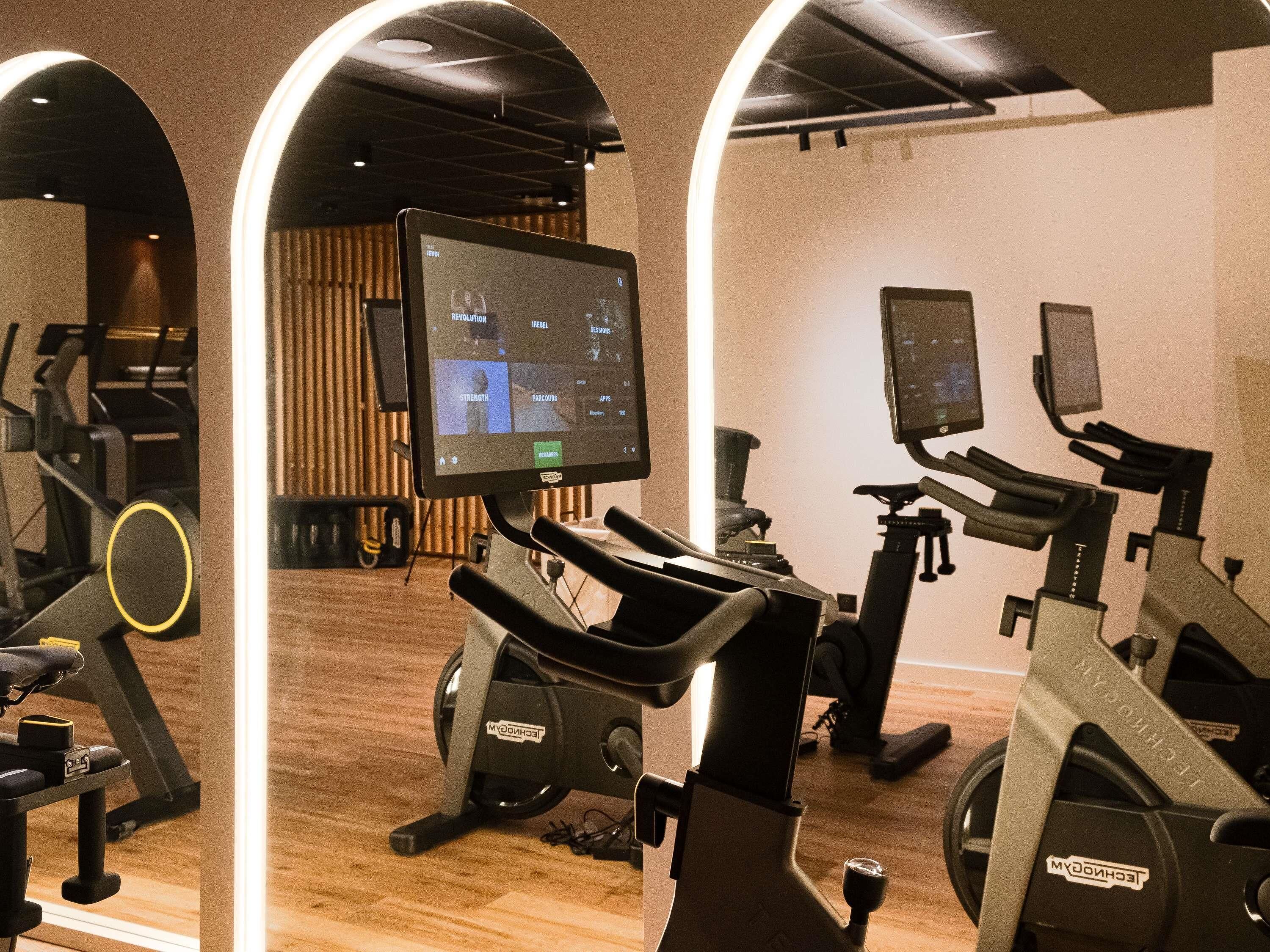 Un gimnasio con bicicletas estáticas, una cinta de correr y un espejo grande.