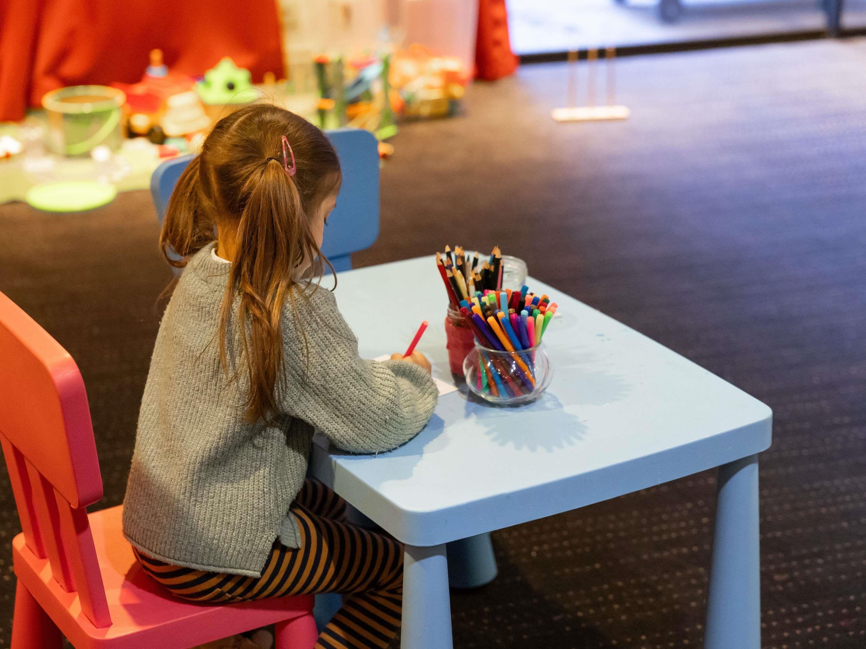 A child sitting at a table with a cup of colored pencils.