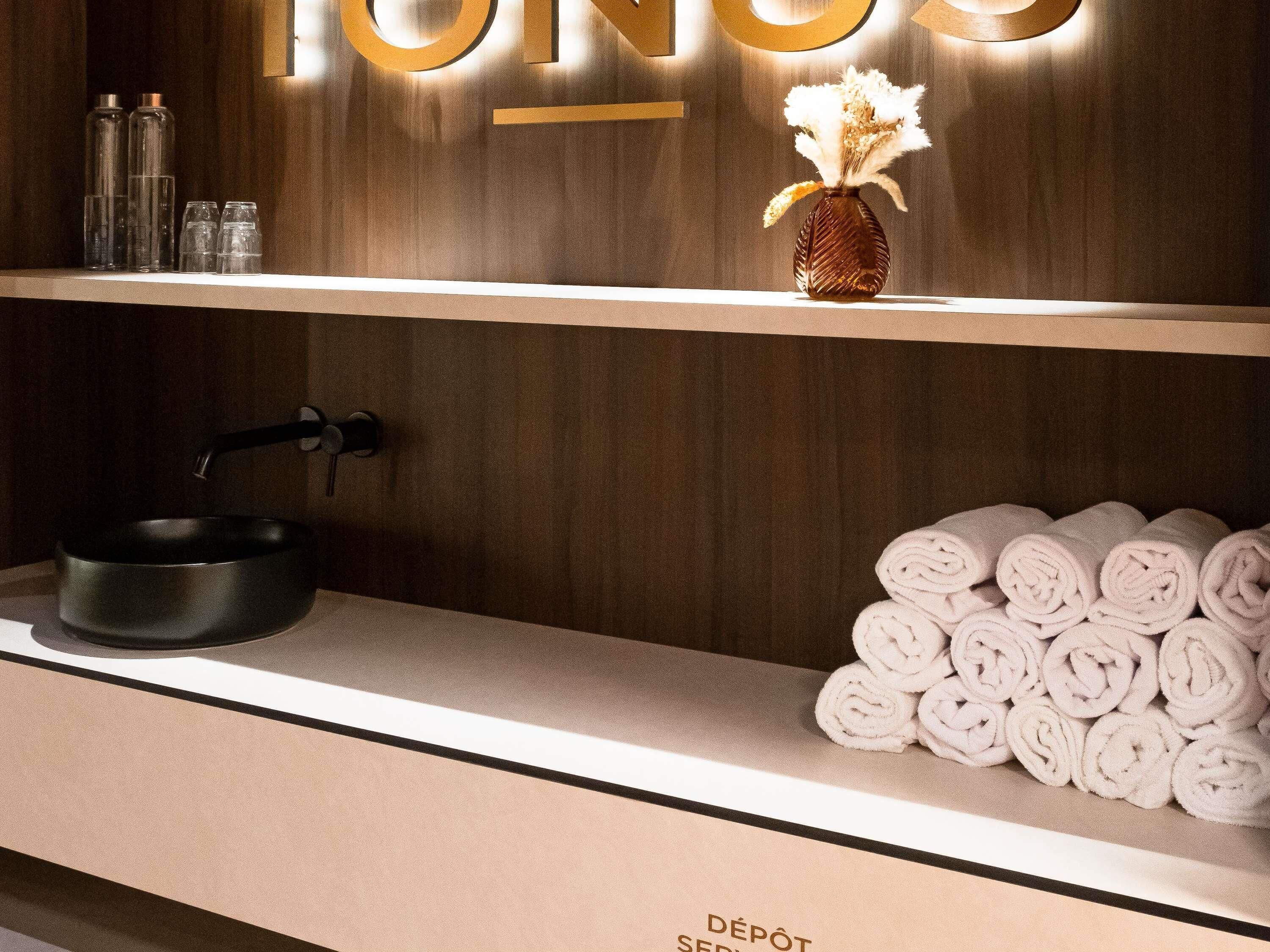 A hotel reception area with a wooden wall, a sink, a towel rack, and a shelf with toiletries.