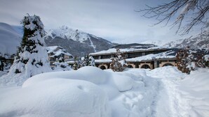 Paisaje montañoso nevado con un edificio que tiene ventanas en arco y un tejado cubierto de nieve.