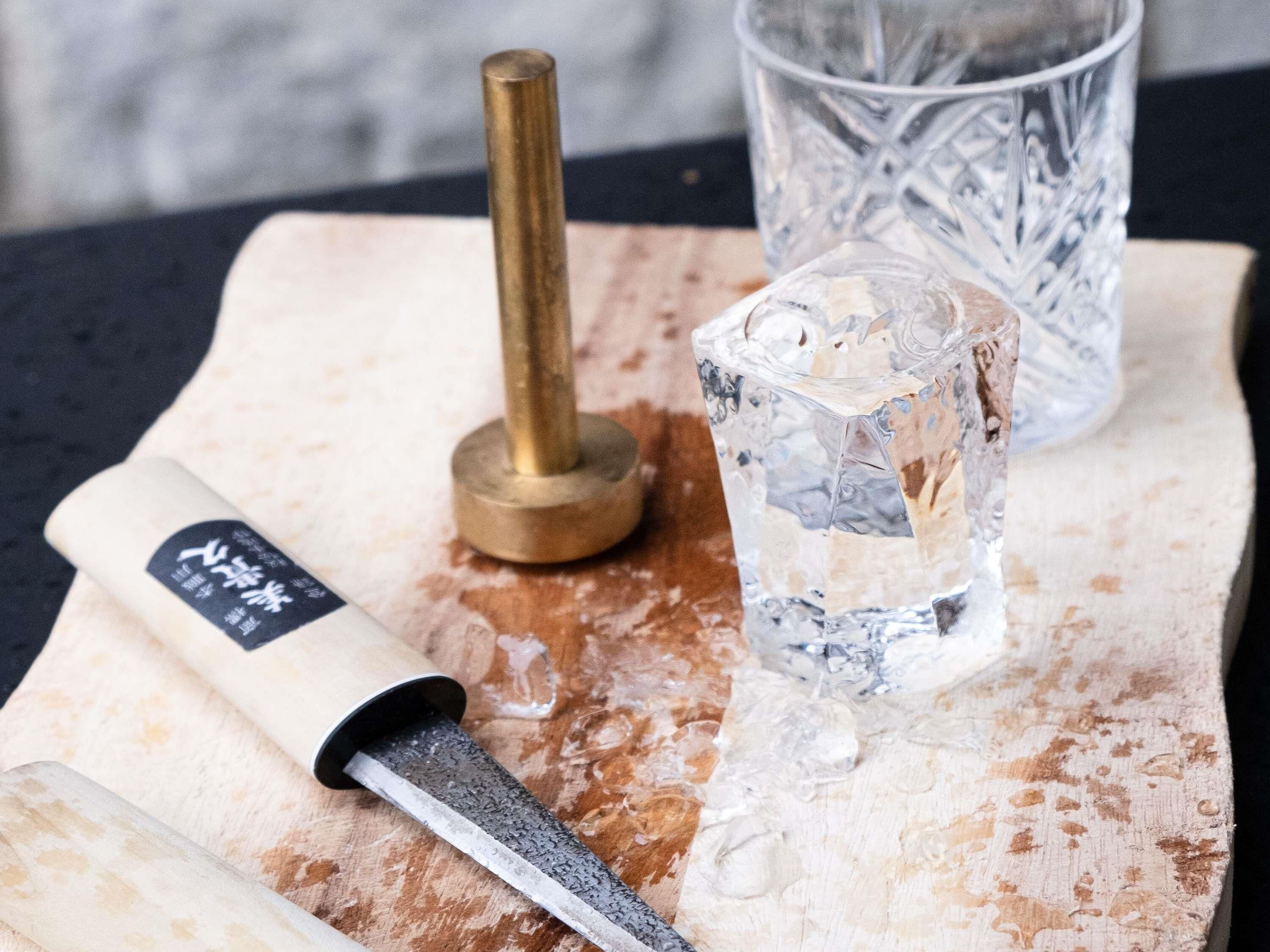 A glass of water, a knife, and a metal tool on a wooden surface.