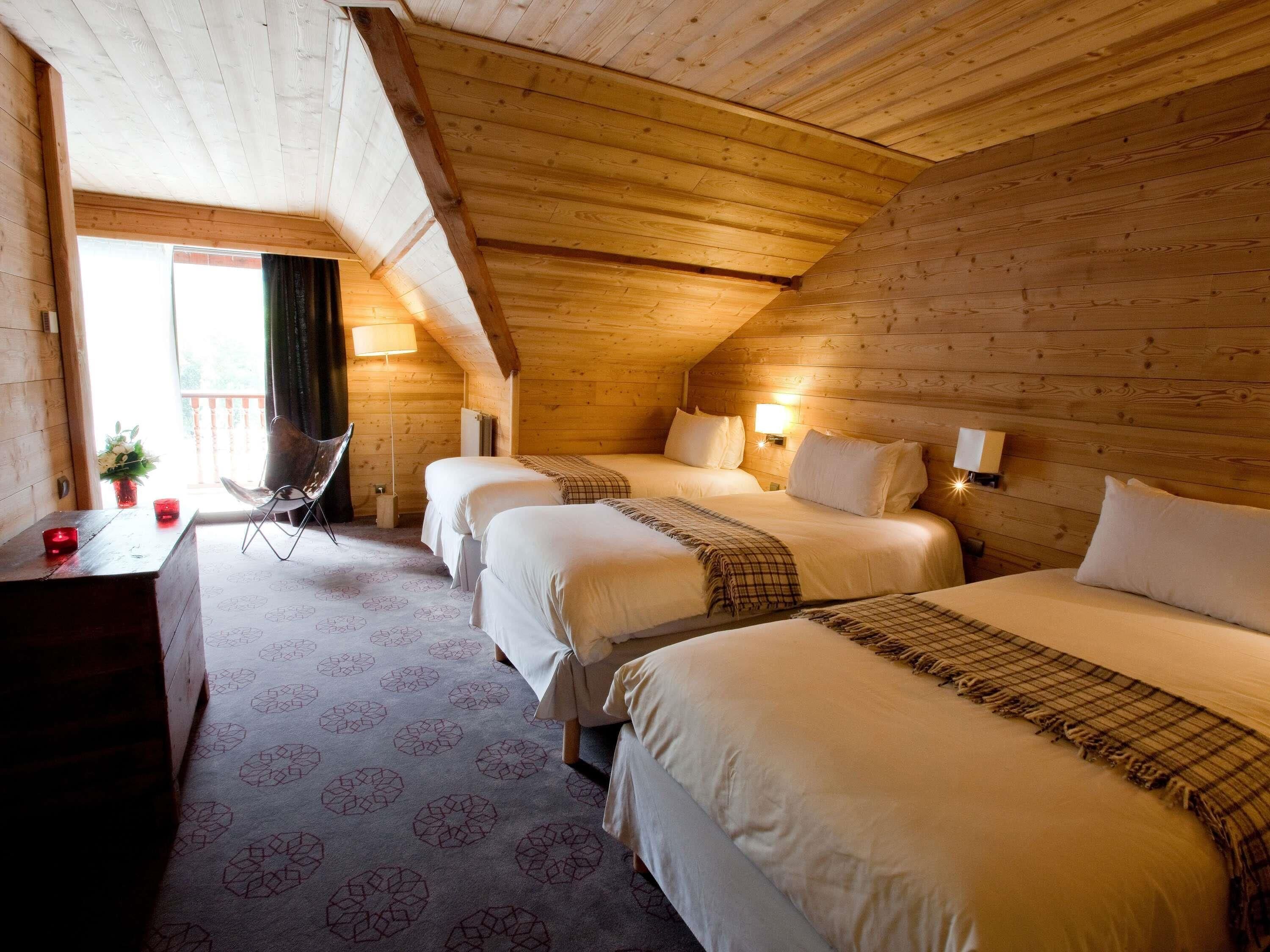 A cozy attic bedroom with two beds, a chair, and a desk.