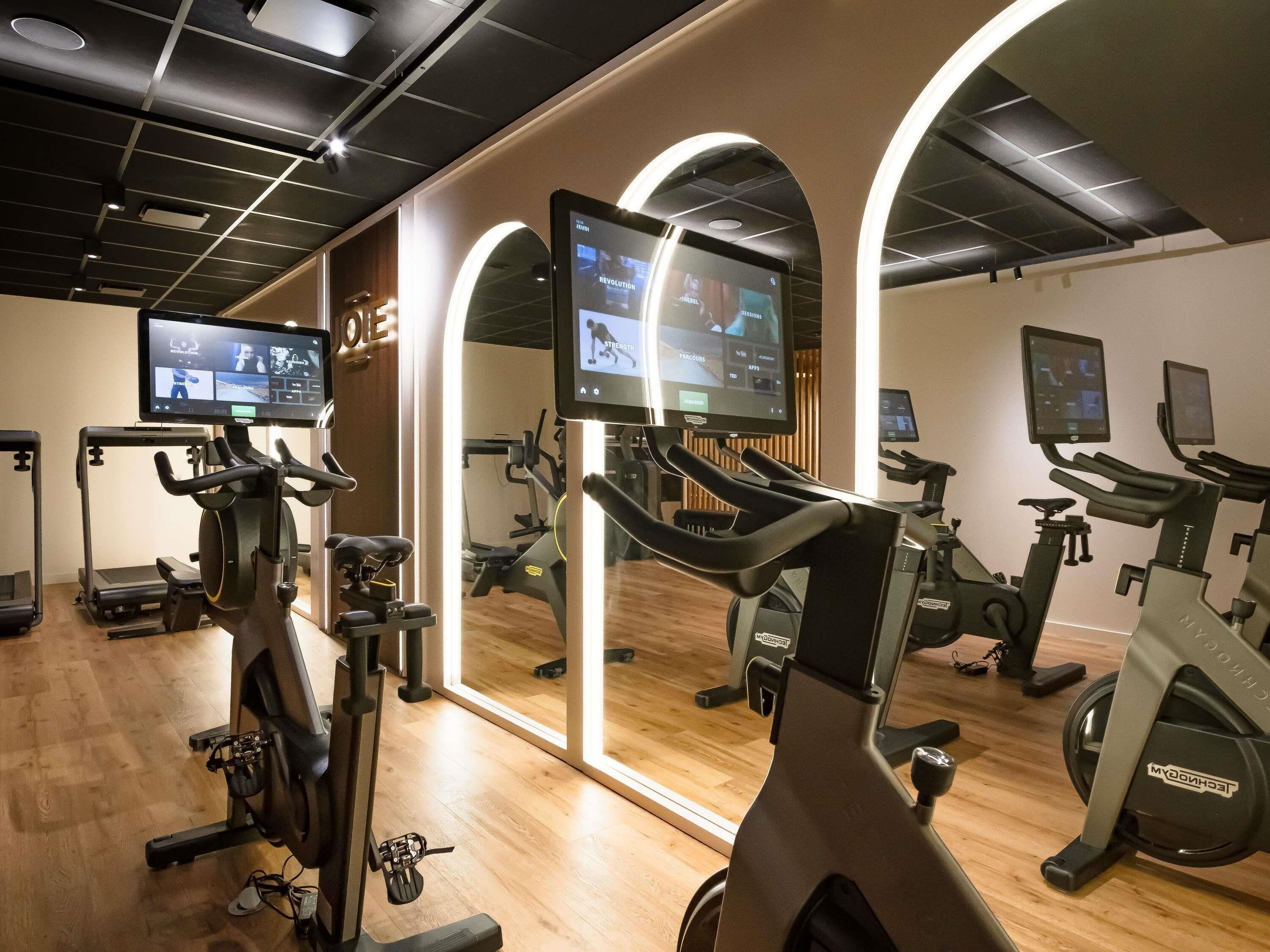 A gym with multiple exercise machines, a mirrored wall, and a digital display.
