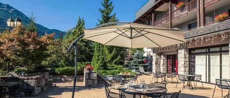 An outdoor patio with tables and chairs, a large umbrella, and a stone wall.