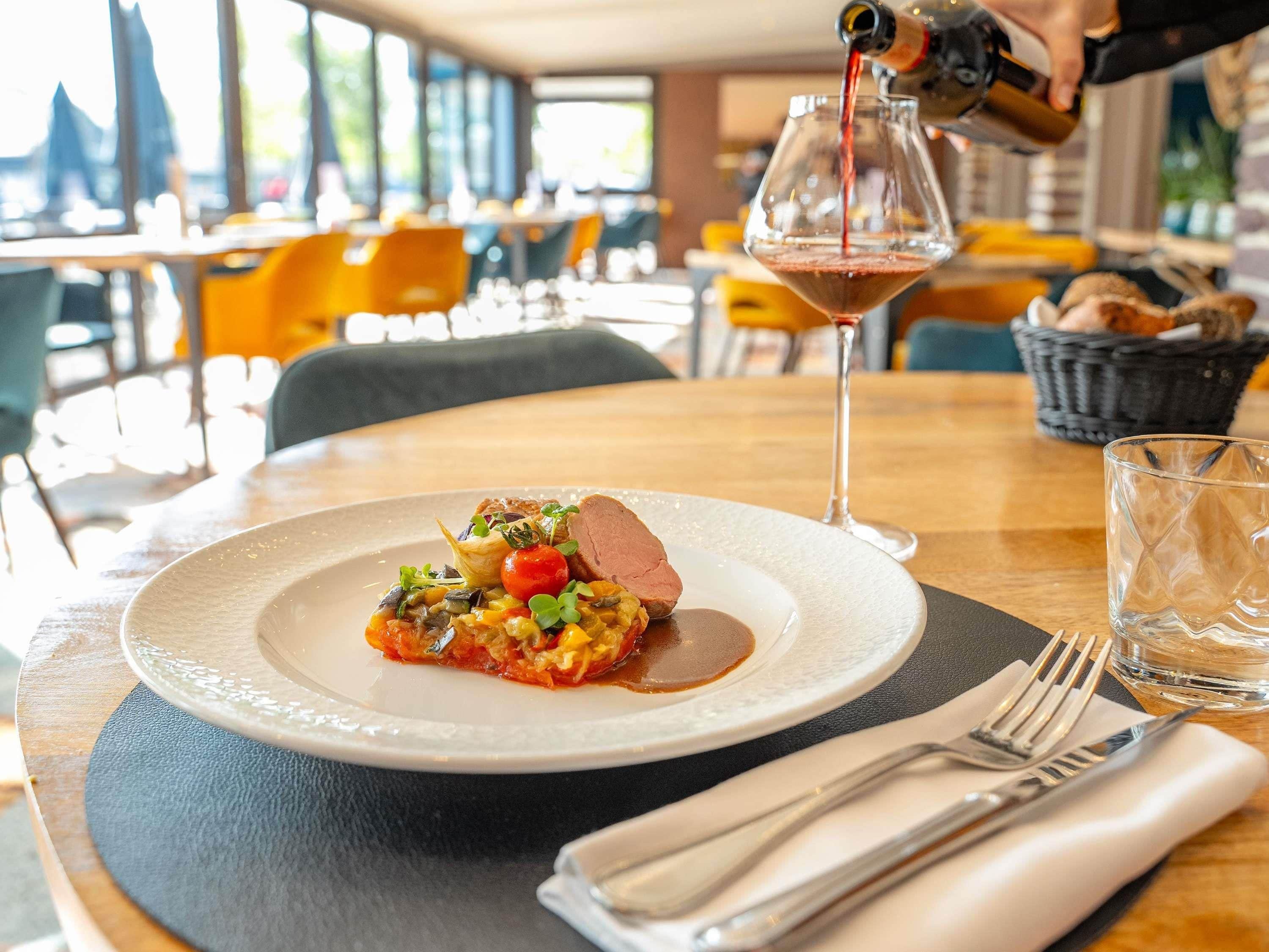 A dining table with a plate of food, a wine glass, and a bottle of wine being poured.