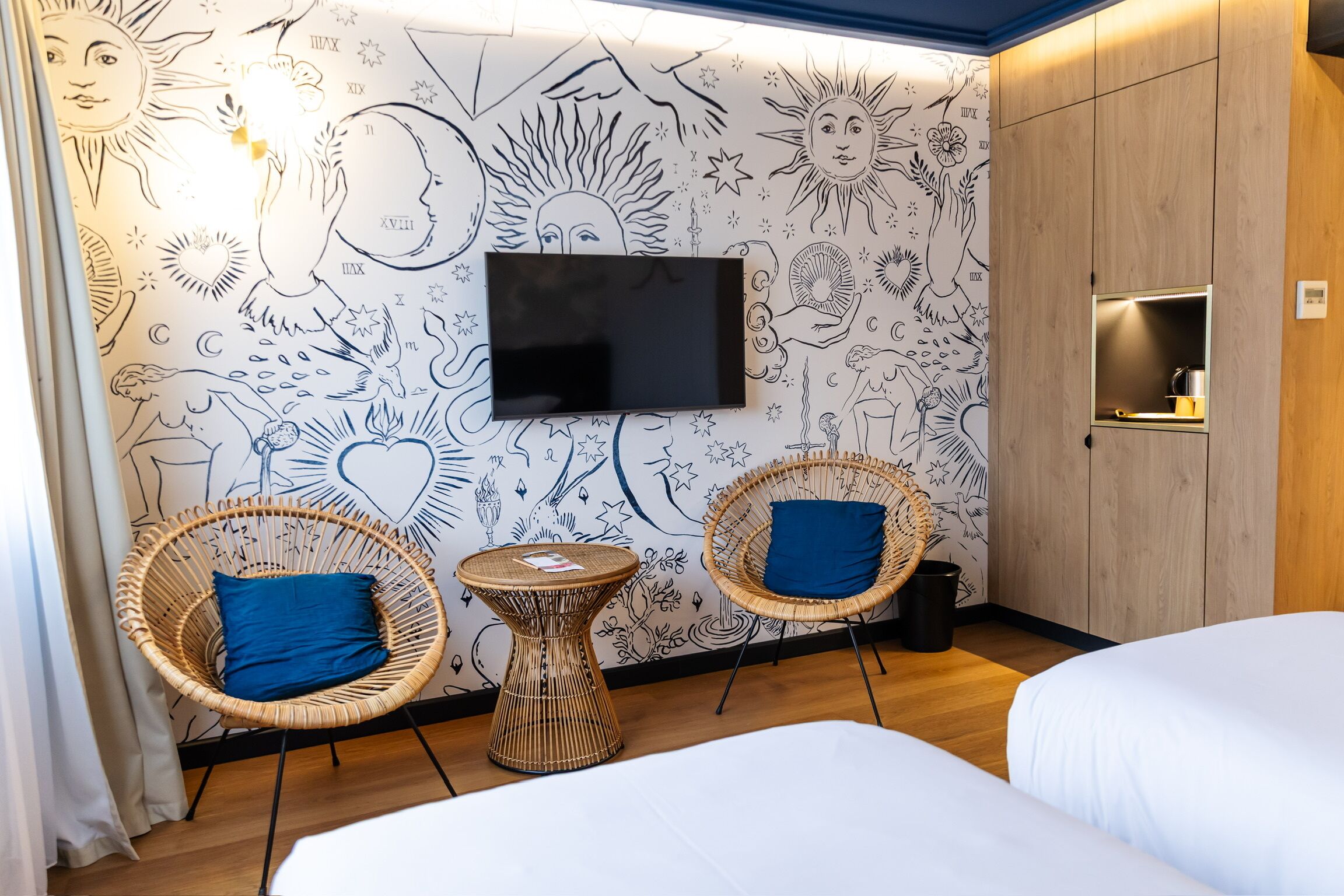 Habitació d'hotel amb dos llits, televisió i una paret amb dibuixos artístics.