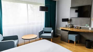 A hotel room with a bed, a desk, a chair, a small table, and a trash bin.